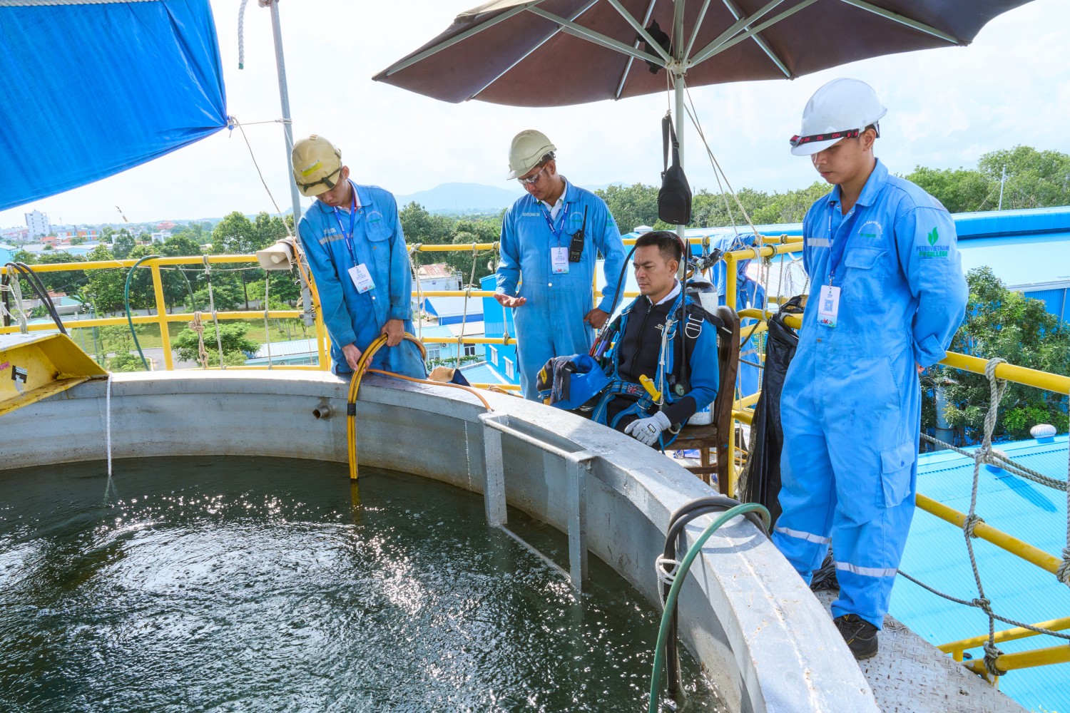 Thí sinh trong trang phục lặn chuyên dụng được đội ngũ hỗ trợ chuẩn bị các điều kiện cần thiết trước khi xuống nước thực hiện bài thi. Công tác chuẩn bị bao gồm kiểm tra tình trạng trang bị bảo hộ, hệ thống cấp khí, phương tiện liên lạc và các dây dẫn phục vụ hoạt động dưới nước. Trong nghề lặn thi công, sự phối hợp chặt chẽ giữa thợ lặn và bộ phận hỗ trợ trên mặt nước giữ vai trò đặc biệt quan trọng, giúp kiểm soát những rủi ro có thể phát sinh và bảo đảm thợ lặn luôn được hỗ trợ kịp thời trong quá trình thực hiện nhiệm vụ.